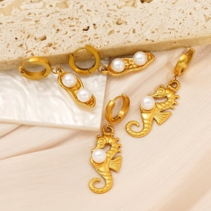 Gold seahorse and pea pod earrings with pearls on a textured stone background