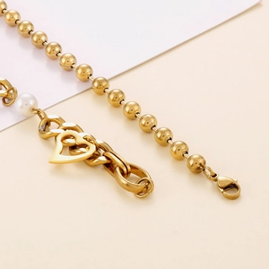 Détail du collier multi-rangs en acier titane doré avec pendentif cœur et perles
