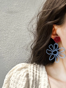 Detail of model wearing red 3D rose and light blue resin cutout flower drop earrings