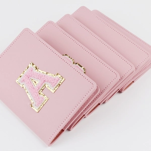 Detail of pink PU leather passport cover with glittery embroidered letter A patch