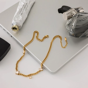 Gros plan d'un collier chaîne cubaine en acier doré 18K orné de quatre zircons carrés