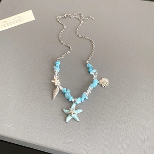 Detail of starfish and shell charms with blue irregular stone beads on a silver necklace