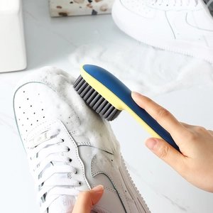 Blue and yellow long handle shoe brush with soft grey bristles cleaning sneakers on marble