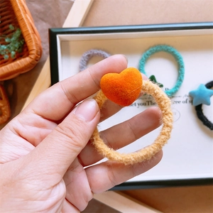 Dettaglio di un elastico per capelli in velluto marrone con cuore arancione morbido
