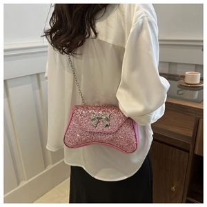 Close-up of pink sequined crossbody bag with silver bow and chain strap on a shoulder