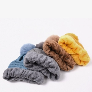 Detail of warm cable knit beanies showing thick faux fur lining and plush pom poms