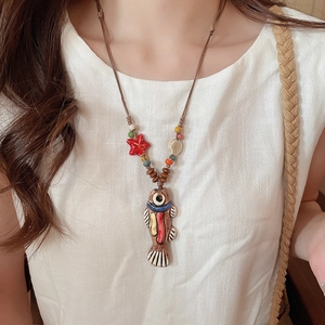 Detail of handcrafted ceramic fish pendant with starfish and wood beads on a woven cord