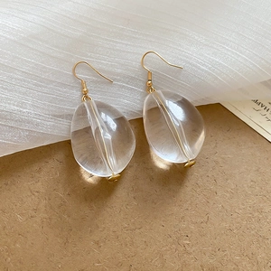 Detail view of acrylic teardrop earrings with gold hooks on a minimalist wooden background