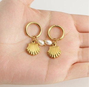 Détail de boucles d'oreilles créoles dorées avec pendentifs coquillages et perles