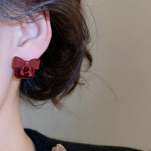 Detail view of red bow earrings with sparkling red zircon worn by a model on a light background