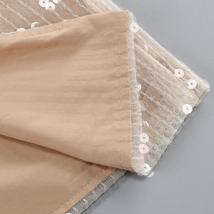Detailed macro shot of sequins on mesh fabric and stitching for apricot evening gown
