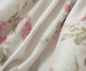 Dettaglio ravvicinato del tessuto in raso beige con rose rosa e foglie verdi del vestito