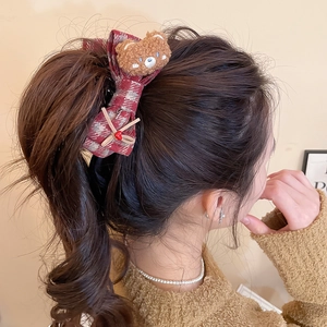 Detailed view of a plaid fabric hair claw clip with a cute brown plush bear on a model