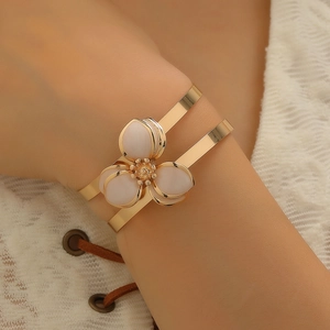 Dettaglio di un bracciale a fiore dorato con petali bianchi e centro in cristallo su modella