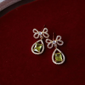 Elegant gold bow-knot water-drop earrings with green gemstones on red velvet background