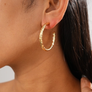 Close-up of a model wearing large gold C-shape hoop earrings with a twisted metal texture