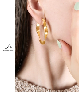Detailed view of large twisted gold U-shaped stainless steel earrings on model