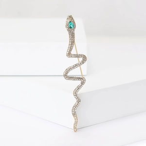 Detailed macro shot of a gold snake brooch with sparkling rhinestones and a green gem