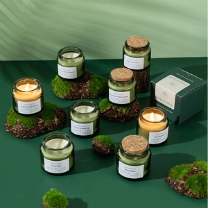 Close-up of scented soy wax candles in green glass jars with cork lids on mossy wood