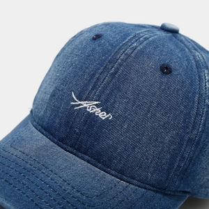 Close-up of white Asher embroidery on blue denim cotton baseball cap with stitching detail