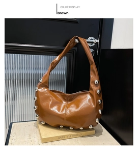 Close-up of brown patent leather shoulder bag with decorative silver metal rivets on base