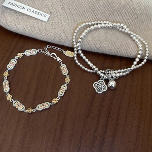 Close-up of silver-toned flower bracelets with orange enamel inlay and metal bell charms