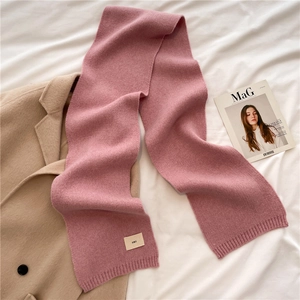 Detail of pink knit scarf with ribbed edges and woven emo label on white fabric