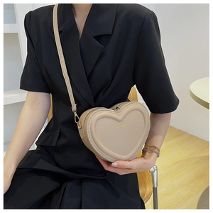 Dettaglio di una borsa a tracolla in pelle beige a forma di cuore indossata da una modella