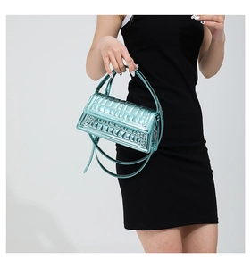 Detailed view of cyan metallic crossbody bag with quilted texture on black dress