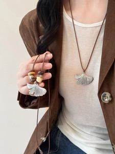 Detail of ginkgo leaf pendant necklaces featuring brown cords and decorative beads