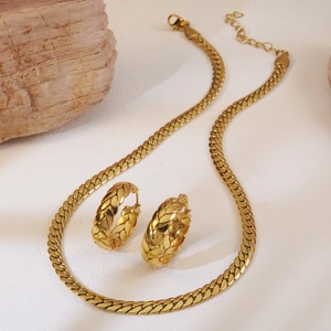 Close-up of golden woven wheat chain necklace and thick hoop earrings set on wood decor