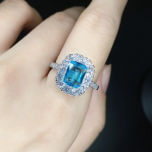 Close-up of emerald cut blue gemstone ring with sparkling diamonds on a finger