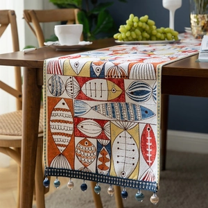 Chenille table runner with fish patterns and tassels on a rustic wooden dining table