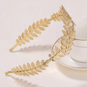 Detail shot of golden metal olive leaf headband placed next to a luxury ceramic cup