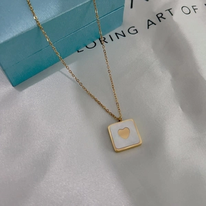 Detail of a gold square necklace with white shell inlay and a central heart pendant