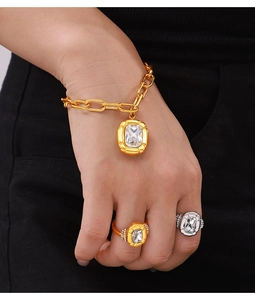 Close-up of gold chain bracelet and rings featuring emerald-cut clear crystal pendants