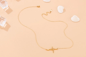 Macro shot of gold heartbeat necklace pendant with adjustable chain on a pink background