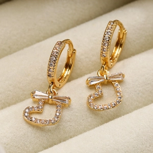 Elegant gold-plated heart drop earrings with zircon bow accents on a velvet display