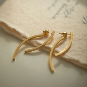Close-up of elegant gold curved bar earrings on minimalist textured beige paper