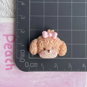 Detailed view of resin teddy dog accessory with pink bow showing size on a cm ruler