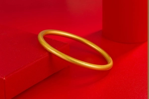 Detailed close-up of matte gold textured bangle resting on luxury red packaging box
