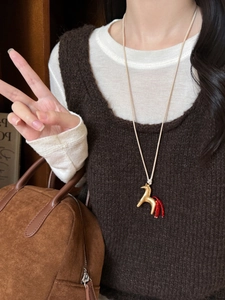 Detail of horse pendant with red beaded tassel on model wearing brown sweater