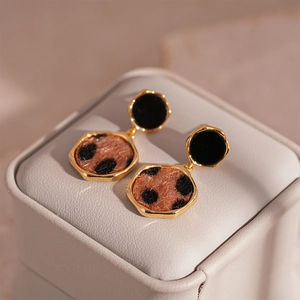 Close-up of golden hexagonal leopard print earrings with faux fur texture on beige box