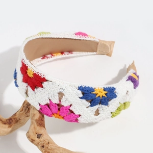 Detail of hand-crocheted white headband with colorful floral embroidery on a wooden branch