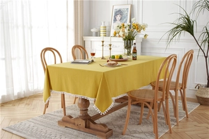 Detail of ginger cotton linen tablecloth with white pompom fringe on wooden dining table