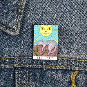 Detail of The Sun Tarot Cat enamel pin with feline sun and kitten on blue denim fabric