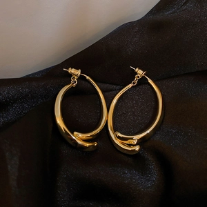 Detail of twisted gold metal hoop earrings on a black silk background in high contrast