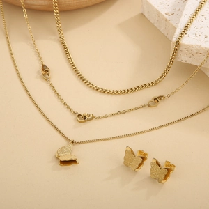 Detail of gold layered necklace set with butterfly and heart pendants on textured stone