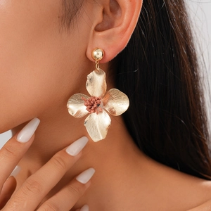 Detail of golden flower earring with textured petals and reddish-brown center on model