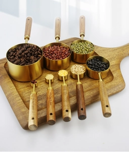 Detail of brass measuring cups and spoons set with acacia wood handles on a board